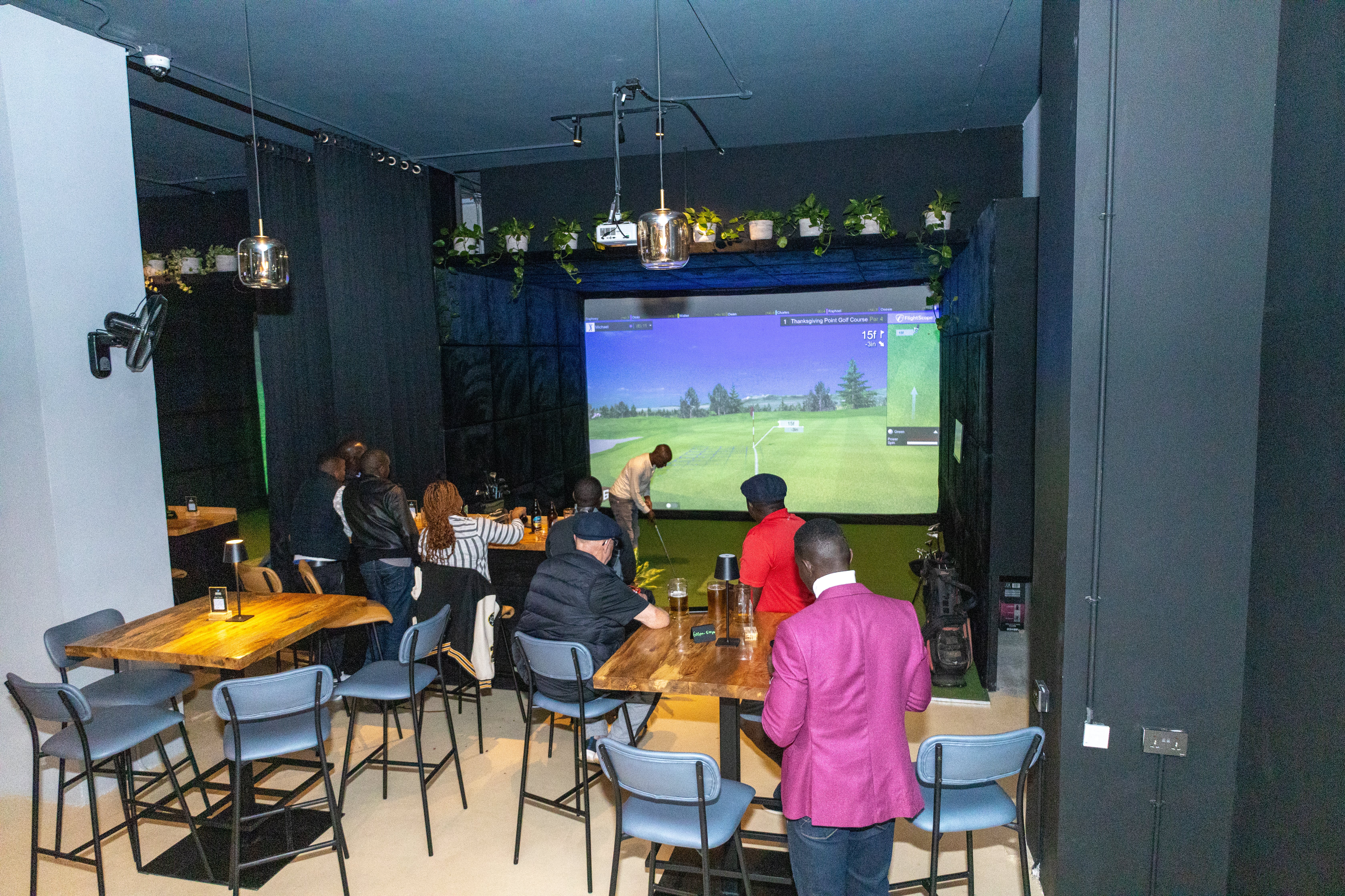 Group of people in a lounge watching a man play on a large golf simulator